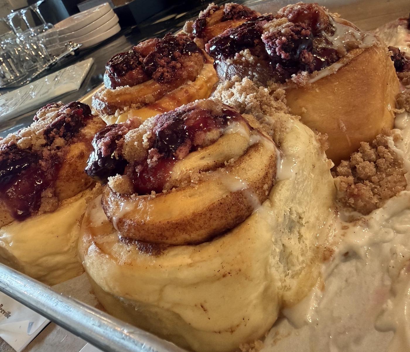 Cinnamon rolls topped with berry compote and streusel, fresh on the tray.